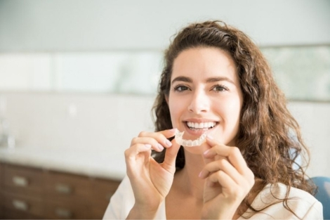 Woman smiling while putting in Invisalign aligners