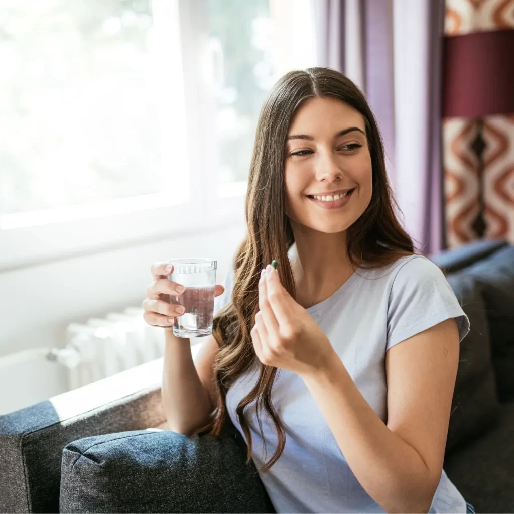 woman smiling holding a vitamin and glass of water